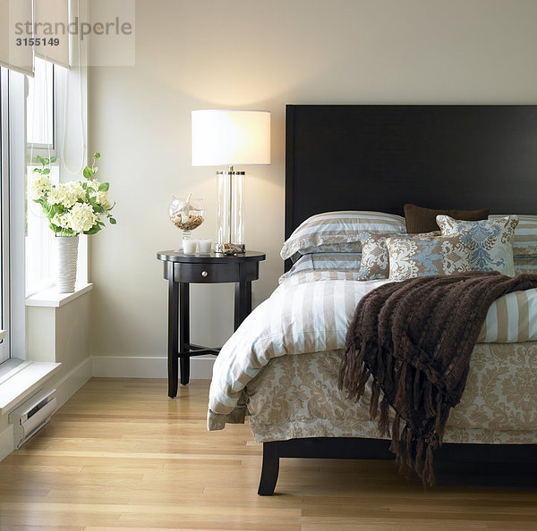 Bedroom with blue and brown bedding  bedside table and hydrangeas in vase  Victoria  British Columbia
