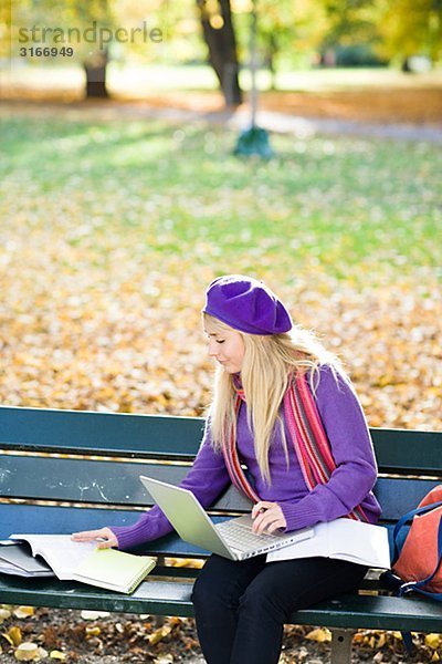 Eine Frau auf Bank in einem Park mit einem Laptop Stockholm Schweden sitzen.