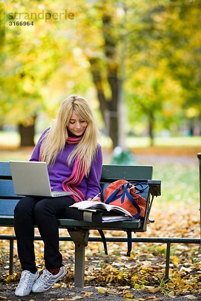 Eine Frau auf Bank in einem Park mit einem Laptop Stockholm Schweden sitzen.
