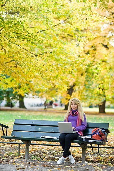 Eine Frau sitzt auf einer Bank in einem Park mit einem Laptop Stockholm Schweden.