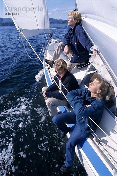 Drei Leute sitzen auf einem Segelboot.