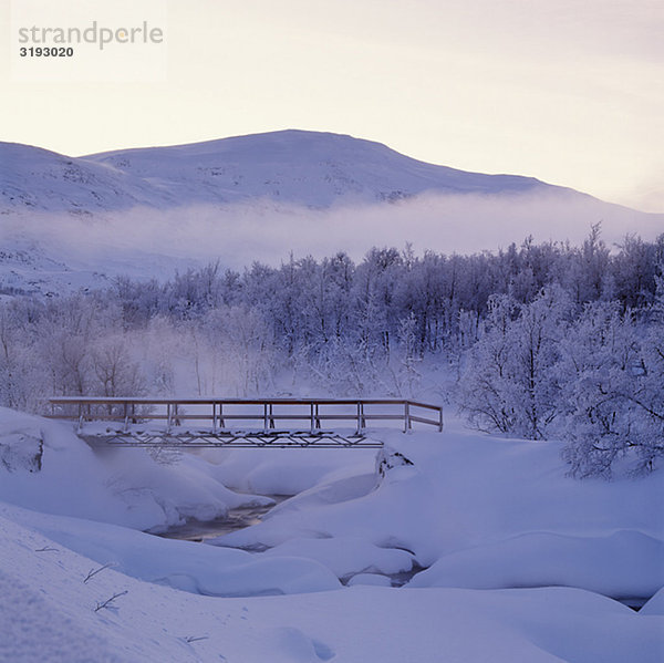 Snow-covered Bridge mit Bäumen und Berge im Hintergrund