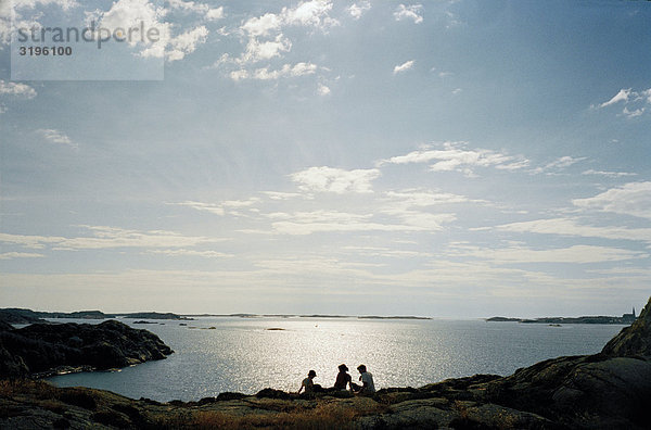 Drei Freunde sitzen auf einer Klippe am Meer  Vastkusten  Schweden.