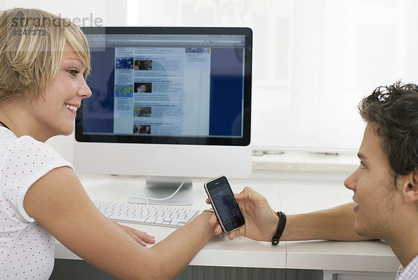 Zwei Teenager in Internetcafe Telefonnummern austauschend  Seitenansicht
