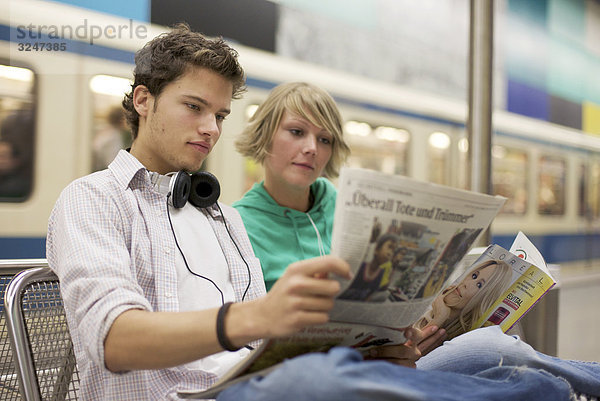 Teenagerpaar Zeitung an U-Bahnstation lesend  Querformat
