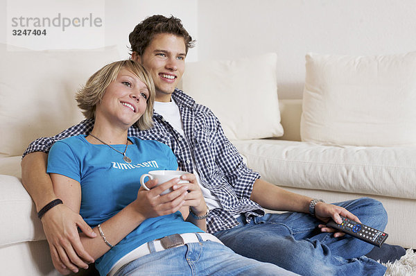 Teenagerpaar vor Couch sitzend und fernsehend  Querformat