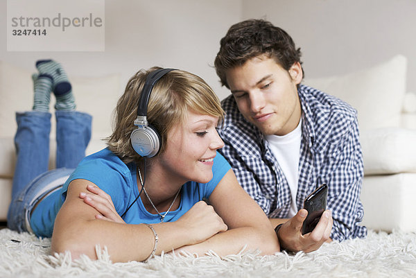 Teenagerpaar auf Flokatiteppich liegend und Musik hörend  Flachwinkelansicht