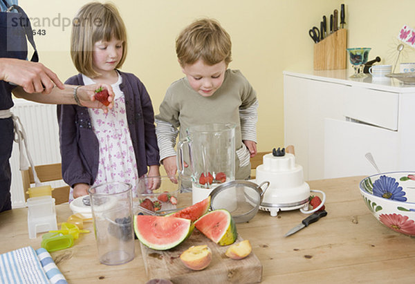 Junge und Mädchen bereiten Fruchtsmoothies zu.