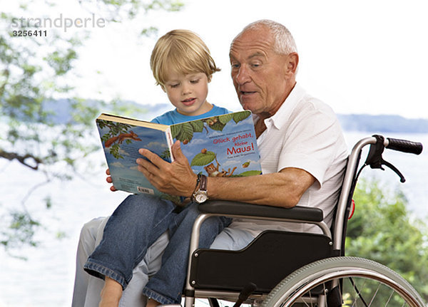 älterer Mann  der dem Jungen das Buch vorliest.