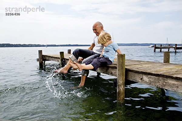 Junge  der mit Großvater am See plätschert.