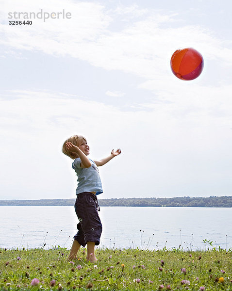 Junge spielt mit Ball am See