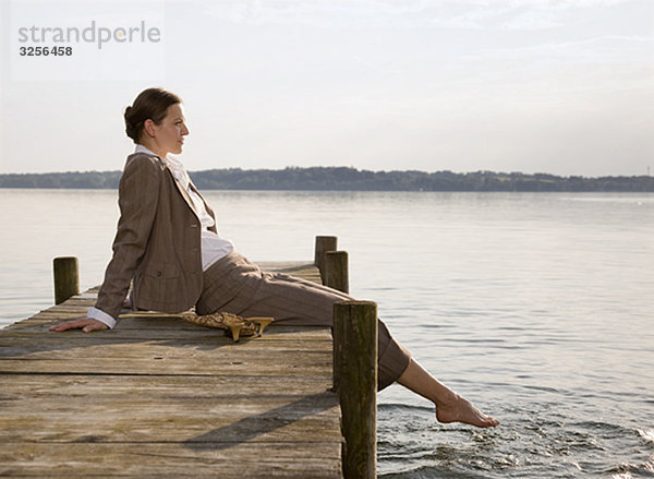 Frau sitzt auf dem Pier am See