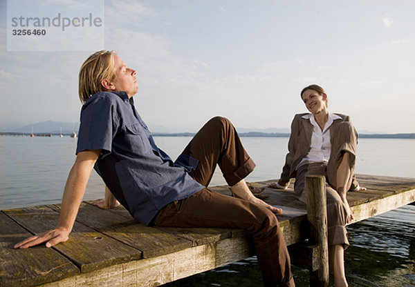 Frau und Mann sitzen auf dem Pier am See