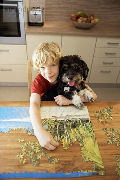 Ein Junge hält einen Hund  während er ein Puzzle macht.