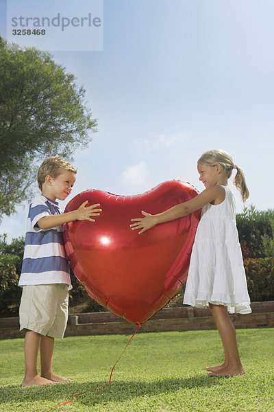 Kleine Kinder umarmen roten Herzballon