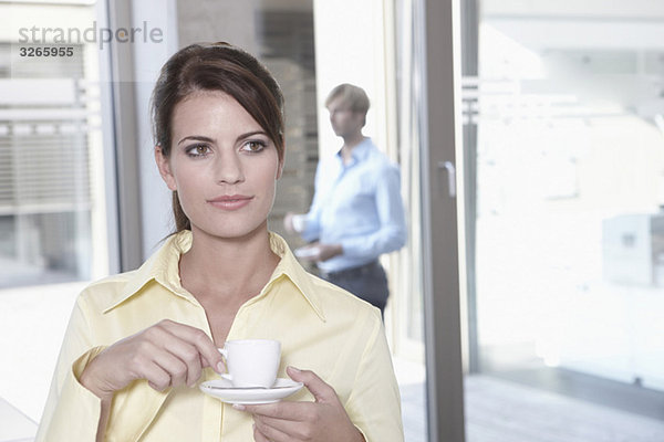 Geschäftsfrau im Büro bei einer Kaffeepause  Geschäftsmann im Hintergrund