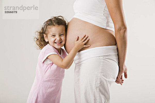 Mädchen (4-5)  das den schwangeren Bauch der Mutter umarmt.