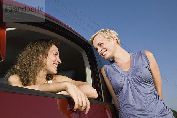 Zwei Frauen  eine von ihnen sitzt im Auto  die andere lehnt sich nach draußen  Porträt  Nahaufnahme