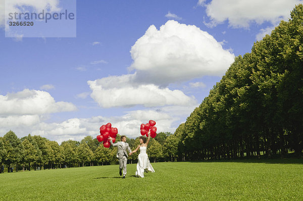Deutschland  Bayern  Brautpaar mit roten Luftballons im Freien