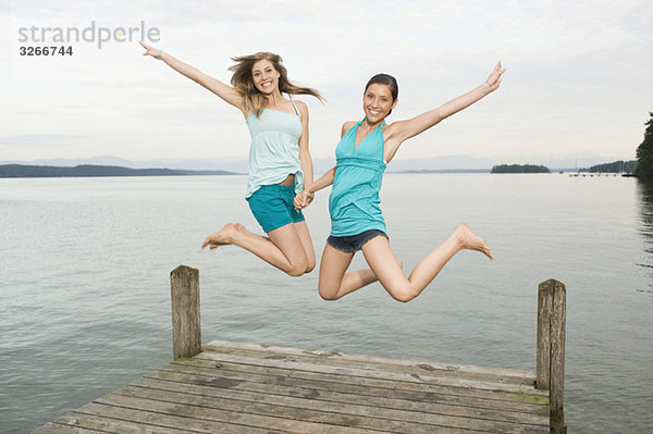 Starnberger See  Zwei junge Frauen springen auf Steg  lachend  Portrait