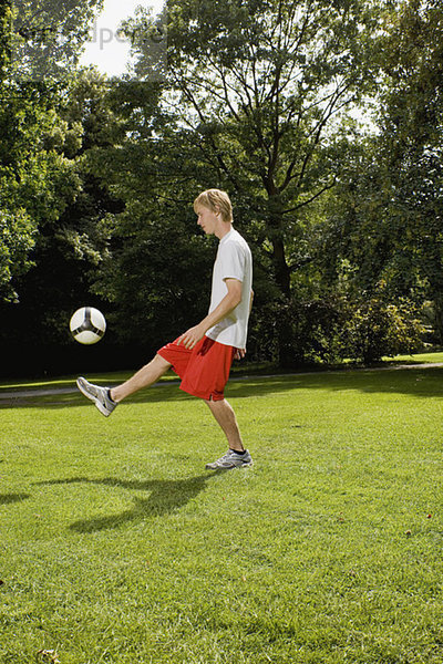 Junger Mann auf dem Rasen  der mit dem Fußball spielt.