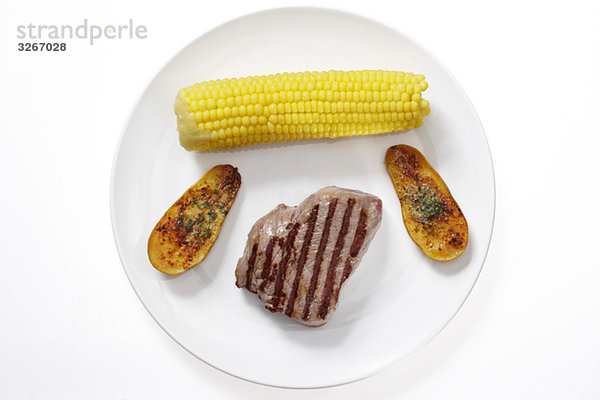 Steak  Maiskolben und geschnittene Kartoffeln auf Teller  erhöhte Ansicht