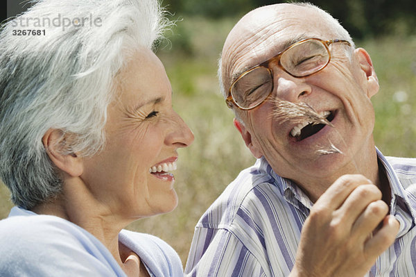 Spanien  Mallorca  Seniorenpaar  Frau kitzelt Mann mit Grashalm  lachend  Portrait  Nahaufnahme