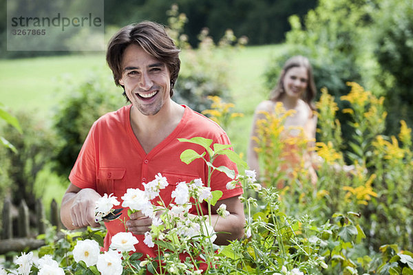 Mann schneidet Blumen  Frau im Hintergrund  lächelnd  Portrait
