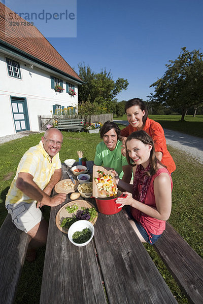 Deutschland  Bayern  Menschen bei Tisch im Garten bei der Zubereitung von Speisen