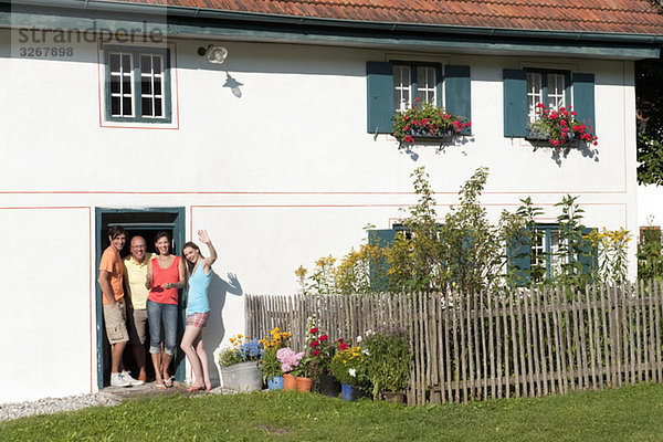 Deutschland  Bayern  Vier Personen winken vor der Haustür  Portrait