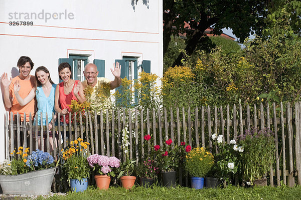 Deutschland  Bayern  Vier Personen stehen am Gartenzaun  winken  Portrait