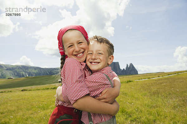 Italien  Seiseralm  Junge (6-7) und Mädchen (8-9) im Feld  umarmend  lächelnd  Portrait