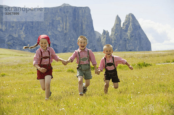 Italien  Seiseralm  Drei Kinder (4-5)  (6-7)  (8-9) beim Laufen im Feld