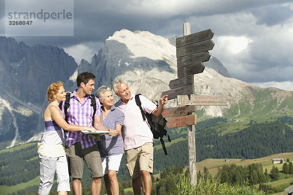 Italien  Seiseralm  Männer und Frauen halten Karte mit Blick auf Wegweiser  lächelnd