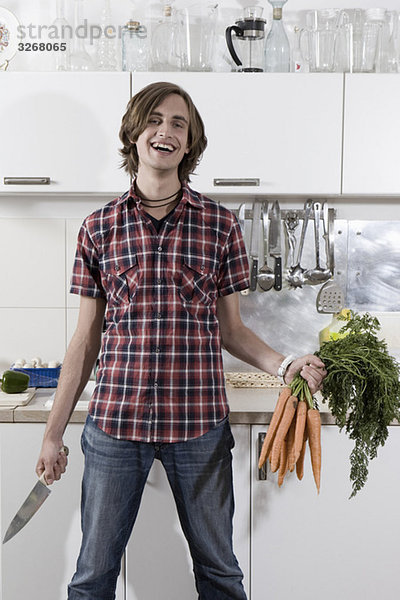 Junger Mann in der Küche mit Karotten und Messer  lächelnd  Porträt