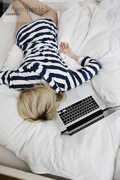 Junge Frau auf dem Bett liegend mit Laptop  Draufsicht