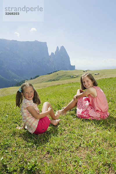 Italien  Südtirol  Seiseralm  Zwei Mädchen (6-7) (10-11) auf der Wiese sitzend