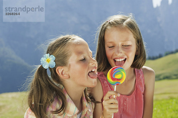 Italien  Südtirol  Zwei Mädchen (6-7) (10-11) lecken Lolli  Portrait  Nahaufnahme