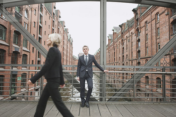 Geschäftsfrau überquert Brücke  Geschäftsmann im Hintergrund an Geländer gelehnt