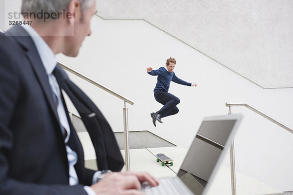 Businesman using laptop  man in background skateboarding