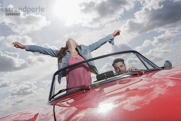Young couple in cabriolet  woman with arms outstretched