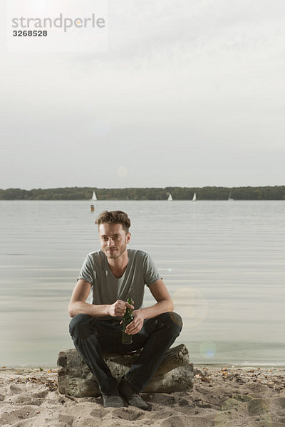 Junger Mann sitzt auf einem Felsen am See  Portrait