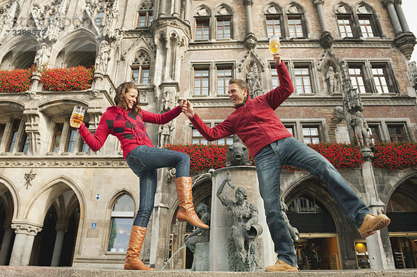 Deutschland  Bayern  München  Marienplatz  Paarbilanzierung am Brunnen  Bierkrüge haltend  lächelnd  Portrait