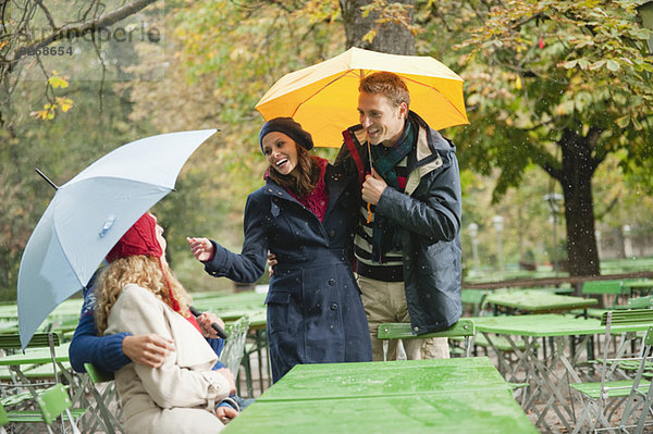 Deutschland  Bayern  Englischer Garten  Biergarten  Vier Personen im verregneten Biergarten im Gespräch