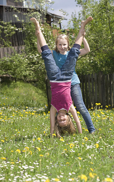 Österreich  Salzkammergut  Zwei Mädchen (10-11) im Garten  Freundin beim Handstand helfen