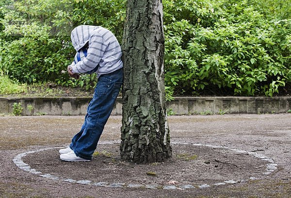 Junge lehnt sich an Baum mit Ball