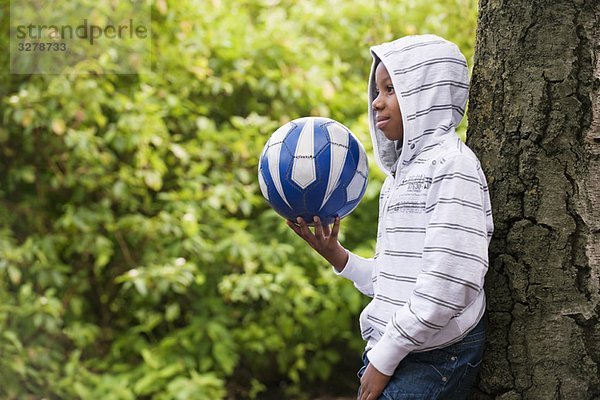 Junge lehnt sich an Baum mit Ball