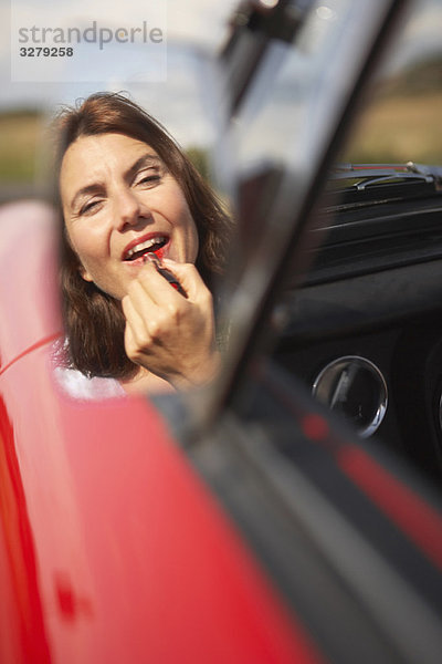 Frau beim Auftragen von Lippenstift im Autospiegel