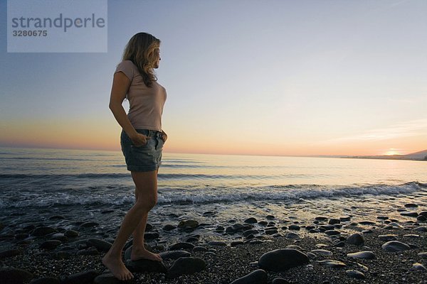 Frau am Strand beobachtet Sonnenuntergang im niedrigen Winkel
