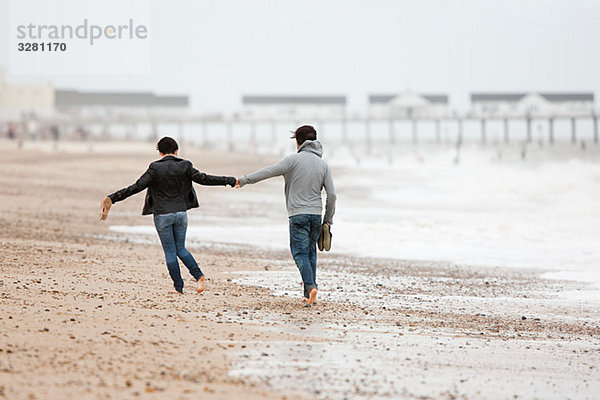 Ein Paar läuft Hand in Hand am Meer.